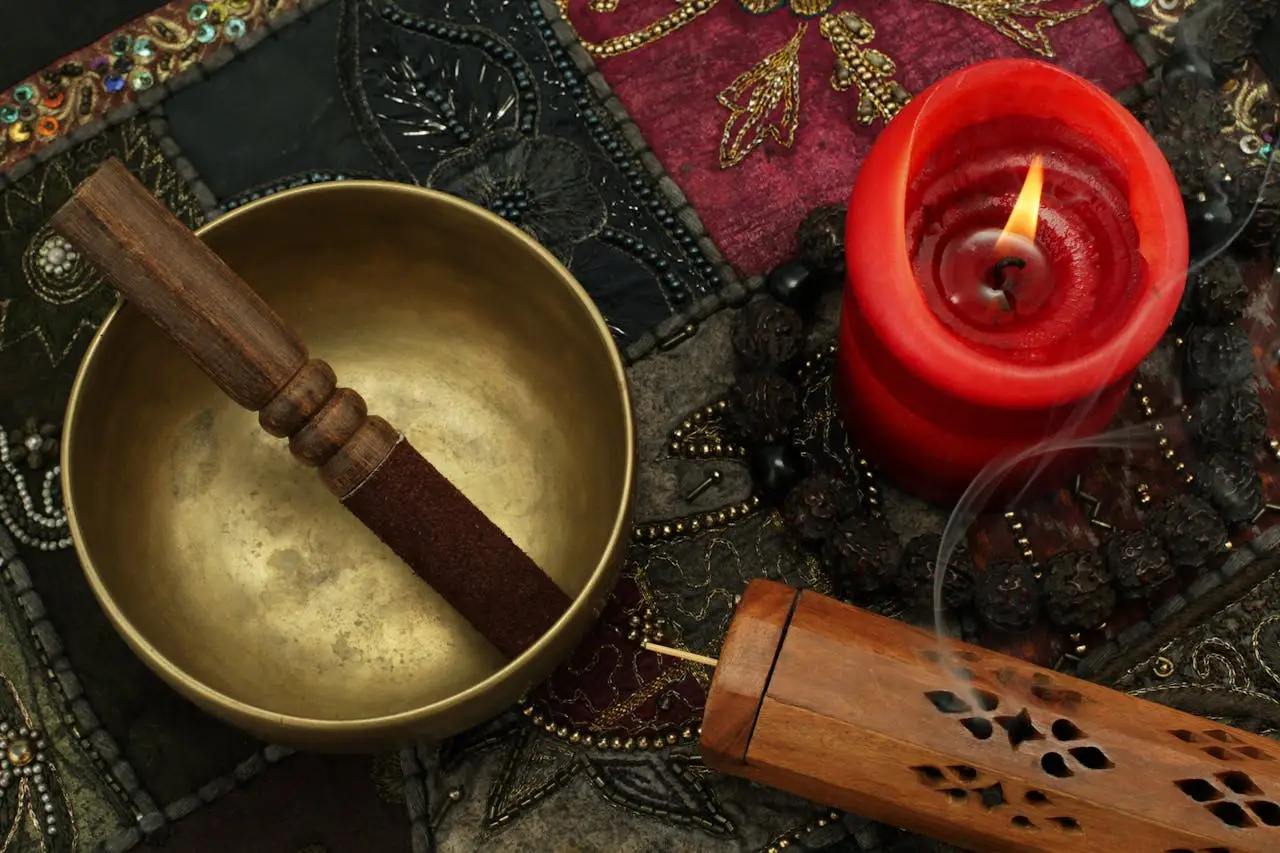 Close-up of a Tibetan singing bowl, candle, and incense on colorful fabric, creating a serene ambiance.